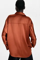 Camisa de manga larga confeccionada en tejido satinado, con cuello solapa, cierre frontal con botones y bajo asimétrico.