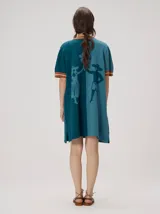 Vestido corto de punto tricolor, con diseño de bloques en tonos turquesa, celeste y azul marino. Presenta cuello redondo y puños con líneas en tonos tostado y blanco, además de un sutil bordado en el pecho.