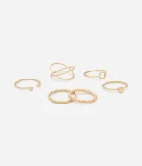 Kit de seis anillos de metal con acabado dorado claro. El conjunto presenta diversos diseños minimalistas y orgánicos, incluyendo un anillo con textura de cuentas, uno de forma ondulada, uno abierto con esferas en las puntas, uno con un pequeño dije circular, uno con un nudo y uno de doble aro entrelazado.