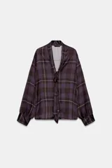 Camisa de tejido satinado con estampado de cuadros en tonos marrones y violetas. Presenta escote en pico con lazo integrado, mangas largas abullonadas y puños ajustados.
