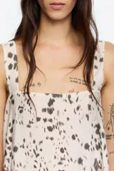 Vestido midi de corte recto, sin mangas y escote cuadrado, con estampado moteado en tonos marrón oscuro sobre fondo beige claro. Lleva un forro o capa inferior de color rojo vibrante que asoma en el ruedo.