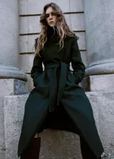 Abrigo largo de paño en color verde oscuro, con cuello alto, cierre frontal oculto y cinturón ajustable del mismo tejido. Presenta un diseño estructurado con bolsillos laterales.