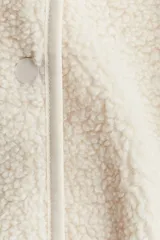 Chaleco de sherpa suave en color beige, con cuello redondo, cierre frontal de botones y bolsillos laterales. Presenta ribetes de cinta finos en los bordes.