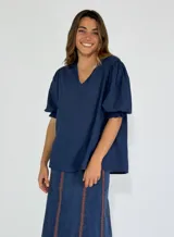 Blusa azul marino con textura de puntos en relieve (tipo plumeti o dobby), escote en V con cuello mao corto y mangas cortas abullonadas con elástico en el puño.