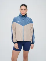 Campera cortaventos Umbro de diseño colorblock en tonos celeste, beige y azul marino, con cuello alto, cierre frontal y bolsillos laterales.