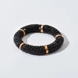 Pulsera rígida tubular cubierta de pequeñas piedras negras brillantes y separaciones con aros dorados.