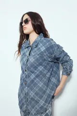 Sobrecamisa de jean con estampado de cuadros, corte relajado, cuello clásico y cierre frontal con botones metálicos.