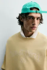 Sudadera de algodón con interior rizo, cuello redondo y manga larga. Presenta un efecto lavado que le da un color amarillo pálido y un estampado frontal en hilo blanco con el texto "west nord 89".