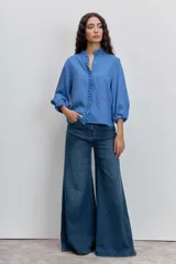 Camisa de manga larga con diseño a rayas verticales en tonos azules. Presenta un cuello mao con detalle de volados a lo largo de la abertura frontal y mangas abullonadas con puños elásticos.