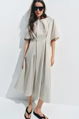 Vestido midi de popelín de algodón en color beige, con cuello redondo, manga corta y pliegues en la cintura. Presenta una falda en línea evasé y cierre en la espalda con cremallera oculta.