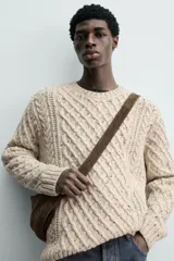 Jersey de punto con diseño de trenzas diagonales, confeccionado en lana con efecto moteado. Presenta cuello redondo, manga larga y terminaciones en rib.