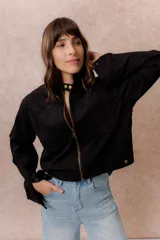 Chaqueta de gamuza sintética color negro, de calce relajado y largo a la cintura. Presenta cuello mao con cierre a presión, cierre frontal metálico, bolsillos delanteros de placa y puños con broche regulable.
