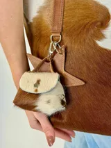 Bolso tipo tote Chabas modelo Molly, confeccionado en cuero con pelo natural en tonos marrón y blanco. Posee asas largas de cuero marrón, parche frontal con la marca grabada y un charm colgante decorativo en forma de estrella con detalle de pelo.