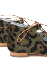 Semibotín de piel de pony con estampado animal print en tonos verde y marrón. Presenta un diseño con aberturas laterales onduladas, cierre de cordones finos y punta afilada. Cuenta con suela de cuero y cuña interna.