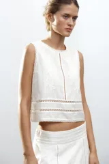 Top blanco de algodón con cuello redondo y sin mangas. Presenta bordados a tono y cierre trasero con abertura y botón.