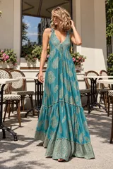 Vestido largo tipo solera de color blanco con estampado paisley en tonos dorados, escote en V y tirantes ajustables con borlas en los extremos. Presenta diseño sin mangas, corte holgado con caída fluida y falda amplia con volados en la parte inferior.