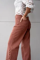 Pantalón de jean color ladrillo, de corte recto y tiro alto, con aberturas laterales en el ruedo y detalle de botones.