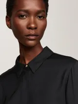 Camisa negra de viscosa con corte amplio, cuello inglés, tapeta de botones oculta, puños abotonados y logo metálico en la manga.