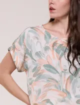 Blusa de silueta holgada confeccionada en crepé liviano, con estampado abstracto en tonos rosados, verdes y blancos. Presenta escote redondo amplio, hombros caídos con hilera de botones decorativos, mangas cortas con dobladillo y ruedo asimétrico en picos.