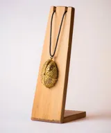 Collar con dije en forma de erizo de mar con textura granulada, suspendido de un cordón negro. El dije presenta un diseño orgánico con pequeños orificios y una superficie detallada.