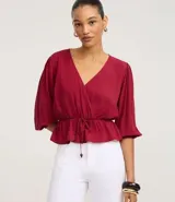 Blusa color vino tinto, con escote cruzado en V, mangas tres cuartos abullonadas con elástico en el puño y peplum ajustado en la cintura con lazo regulable.