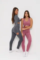 Conjunto deportivo de dos piezas compuesto por un top de manga larga tipo crop top con aberturas para pulgares y una calza de tiro alto. Ambas prendas presentan un diseño seamless con detalles de texturas perforadas y el logo de la marca estampado en el frente.