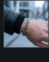 Pulsera de eslabones de acero inoxidable con placas hexagonales decoradas con el símbolo de la flor de lis en relieve y acabado envejecido. Cuenta con un cierre de mosquetón robusto.