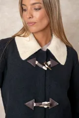 Montgomery de lana color negro con cuello de punto en color crema, cierre frontal con alamares y bolsillos con solapa.