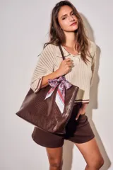 Bolso tipo shopper color marrón de cuero sintético con diseño trenzado. Cuenta con doble asa de hombro y placa metálica con el logo de la marca en el frente.