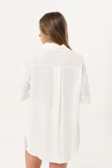 Camisa blanca de silueta oversize, con cuello camisero, manga 3/4 y corte más largo en la espalda. Presenta bordados de coral y caracol en el frente, y botones a tono.