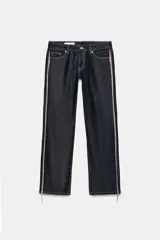 Jeans de tiro bajo y corte recto en denim color azul oscuro. Presenta cinco bolsillos, trabillas para cinturón y cierre frontal con cremallera y botón metálico. Destaca por la aplicación de flecos brillantes en los laterales de ambas piernas.