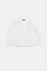 Camisa blanca con cuello solapa, escote pico y mangas tres cuartos abullonadas con elástico en el puño. Presenta bordados perforados (ojales) con diseño floral en toda la prenda.