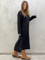 Vestido midi de punto en color gris oscuro, con diseño de rombos en relieve, cuello en V, mangas largas y abertura lateral con botones decorativos.