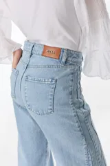 Pantalón de pierna ancha con acabado brillante, confeccionado en lino. Presenta un diseño de tiro medio con cierre de botón y cremallera, bolsillos traseros y etiqueta de marca en la cintura.
