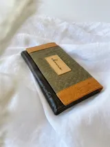 Billetera de cuero con diseño tricolor en tonos verde, marrón y negro, con textura tipo reptil. Presenta un parche central con la marca grabada y cierre con broche.