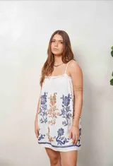 Vestido corto color beige de corte holgado, con tirantes finos y diseño sin mangas. Presenta bordados florales en tonos azules y marrones en todo el frente y un detalle bordado en el borde inferior.