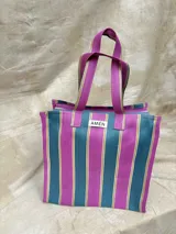 Bolso tipo tote de plástico reciclado, con diseño a rayas verticales color fucsia, azul y amarillo. Tiene cierre y bolsillo interior.