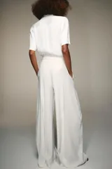 Camisa de cuello solapa y manga corta, confeccionada en tejido satinado. Presenta falsos bolsillos con solapa en el delantero, bajo asimétrico y cierre frontal con botones.