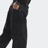 Pantalón cargo de denim negro con corte holgado, bolsillos laterales tipo cargo y cierre frontal con botón y cremallera.
