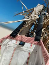 Bolso tipo tote rayado en tonos rosa y blanco, con asas cortas negras y correa larga regulable negra.