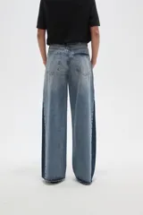 Pantalon de jean de corte ancho con diseño color block, combinando paneles de denim lavado claro en el centro y denim azul oscuro en los laterales. Presenta tiro medio y terminaciones deshilachadas en el ruedo.