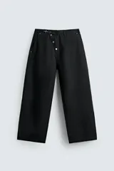 Pantalón wide fit de algodón con efecto lavado, corte recto y holgado. Presenta un cierre frontal cruzado con botones y un alamar metálico distintivo, además de bolsillos frontales y traseros de plastrón.