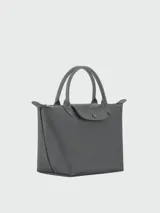 Cartera de mano tipo tote, modelo Le Pliage One, confeccionada en material sintético resistente con detalles en cuero. Presenta un diseño minimalista con cierre superior, solapa frontal con botón a presión y doble asa corta.