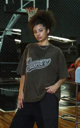 Remera de manga corta y cuello redondo, calce oversize, color marrón oscuro con efecto batik artesanal (lavado ácido). Estampa frontal con la palabra "Ravers" en estilo cursiva con contorno blanco.