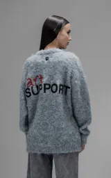 Sweater de punto texturizado color gris, con cuello redondo y diseño oversize. Presenta un bordado en relieve en la espalda con la frase 'art SUPPORT' en letras rojas y negras.