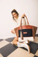 Bolso tipo shopper de gran tamaño, confeccionado en una combinación de lona y gamuza. Presenta un diseño tricolor con paneles en negro, blanco y marrón, con detalles en cuero marrón y borlas decorativas colgantes. Incluye doble asa de hombro y cierre principal.