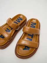 Sandalias de cuero vacuno color marrón con acabado brillante, diseño de dos tiras anchas acolchadas y plataforma baja.