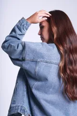 Campera clásica de jean celeste con cuello camisero, bolsillos frontales con solapa y cierre con botones metálicos. Presenta detalles de pequeños brillos blancos dispersos en la parte delantera y las mangas.