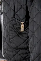Campera corta de diseño capitoneado con patrón de rombos, color negro. Presenta cuello redondo, cierre frontal abierto, mangas largas y dos bolsillos delanteros con detalle de broche.