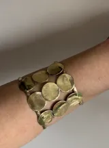 Brazalete rígido de bronce dorado con apliques circulares.